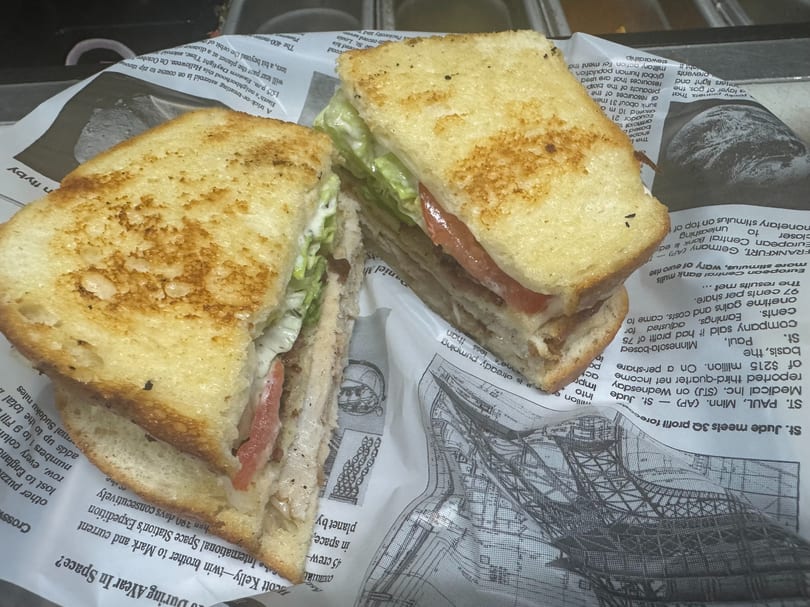 A grilled sandwich, cut in half, with lettuce, tomato, and meat, served on newspaper.