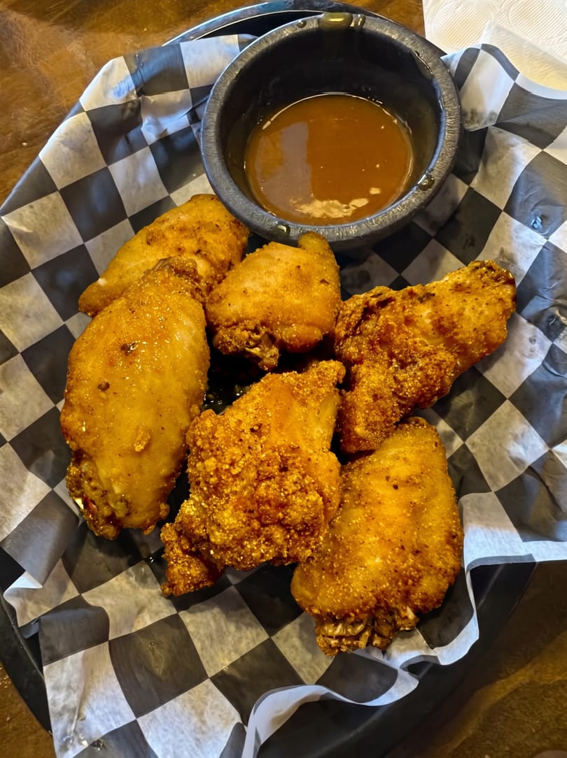 Crispy fried chicken wings and a small bowl of dipping sauce on checkered paper.